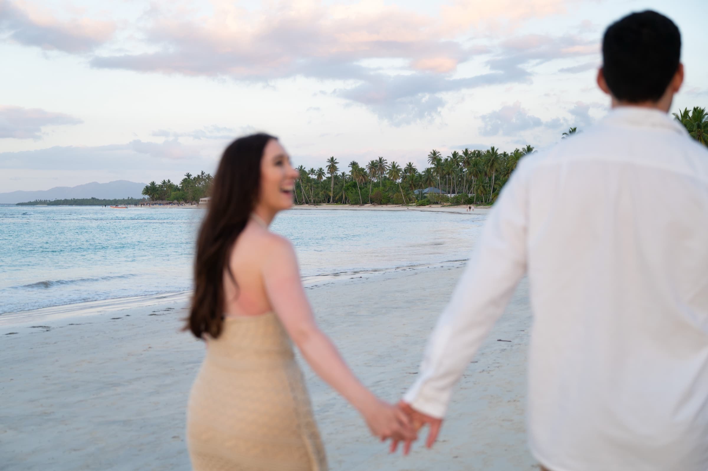 A couple walking hand in hand along the beach at dusk