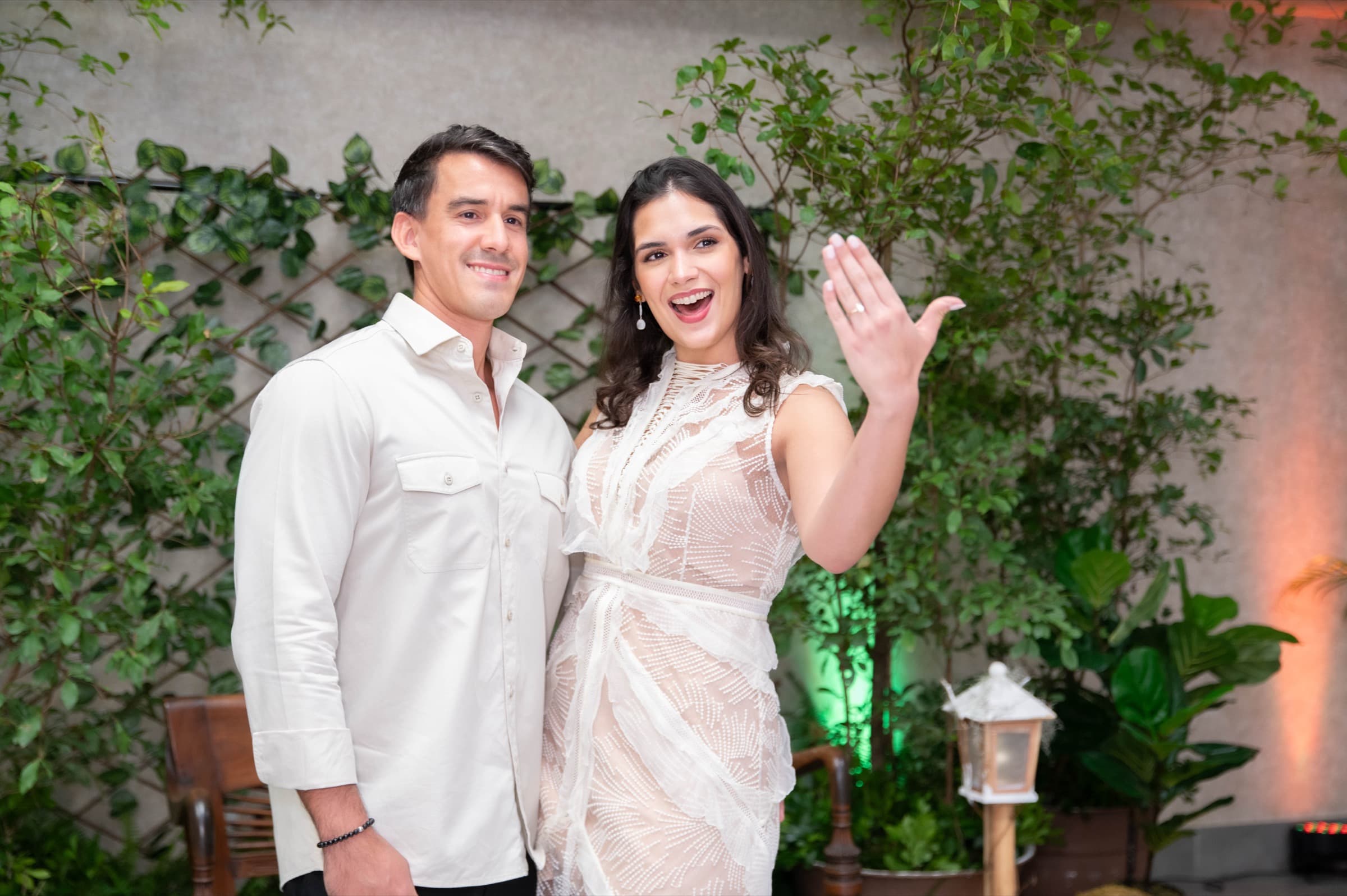 Chantal & Luis laughing together as she shows off her ring among the greenery