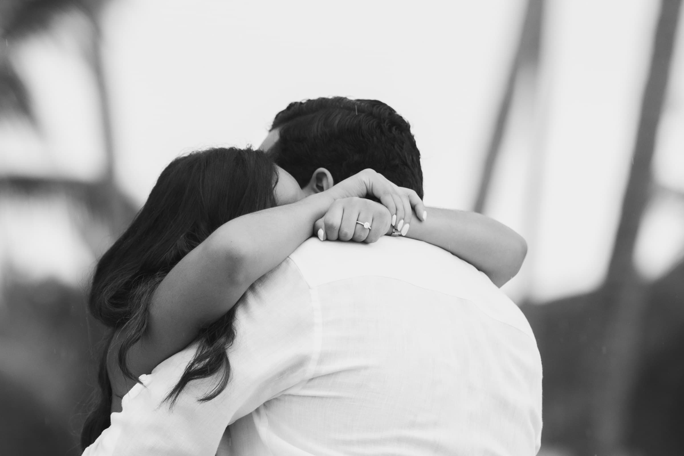 An embrace from behind, the new ring resting on his shoulder, black and white