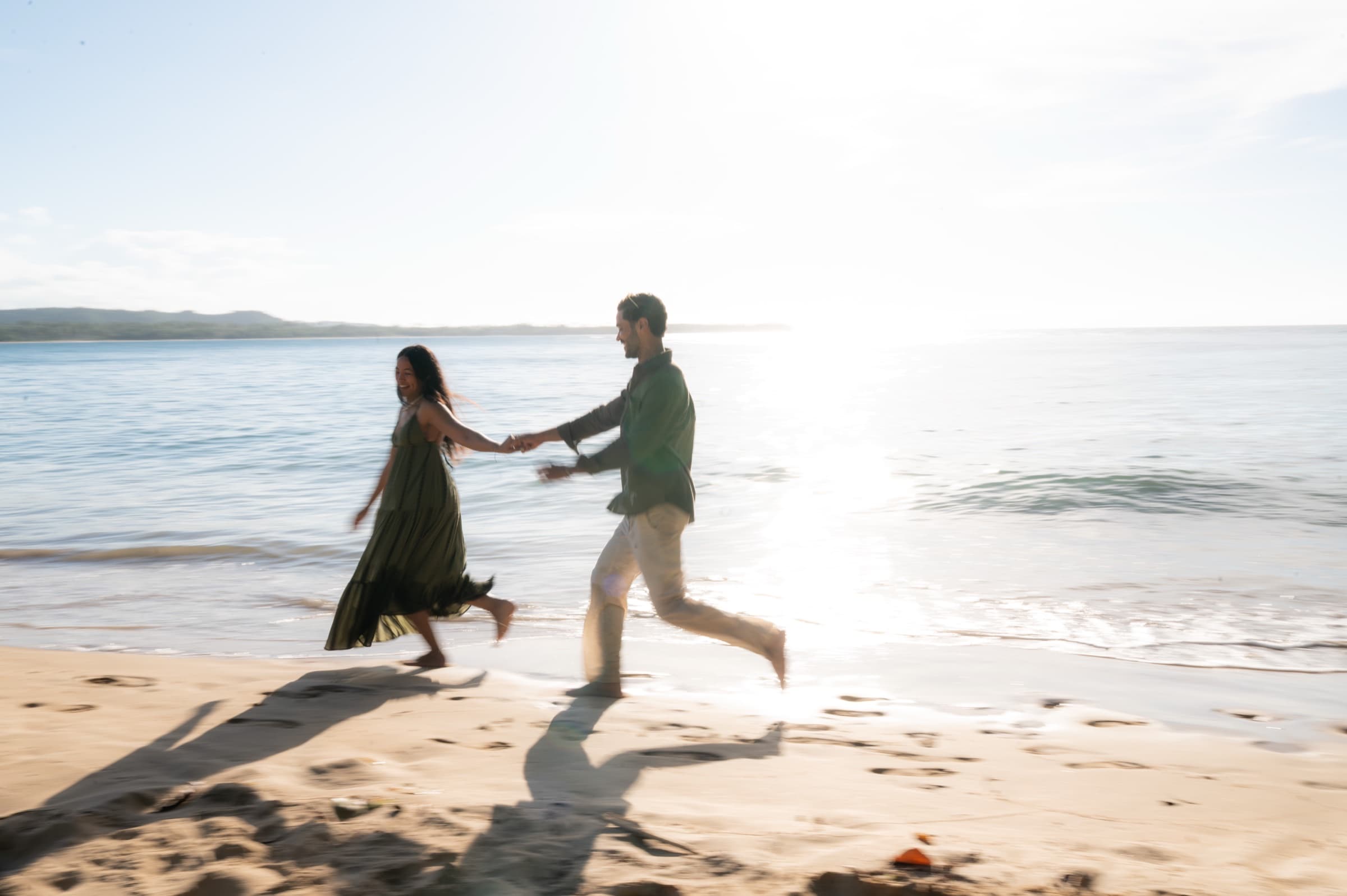 Franchesca & Linero running hand in hand along the shore at sunset